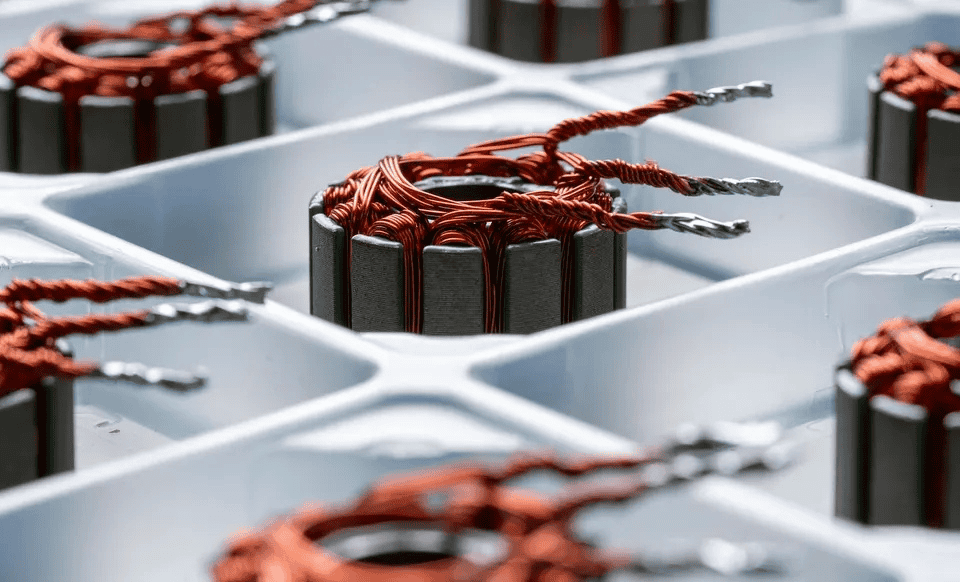 Close-up of copper wire coils wound around metal cores, organized in a plastic grid tray—likely components for electric motors or transformers, as used in AI engineering automation and defense startup applications.